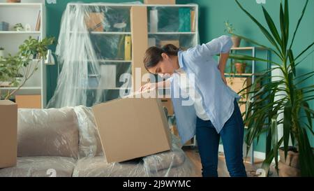 Une femme ressent une douleur soudaine au dos lorsqu'elle tente de soulever une boîte à carton. Banque D'Images