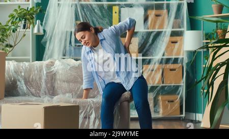 Une femme ressent une douleur soudaine au dos lorsqu'elle tente de soulever une boîte à carton. Banque D'Images