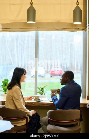 Vue arrière d'un couple d'affaires multiethnique qui boit du café ensemble et parle pendant la réunion au café-restaurant Banque D'Images