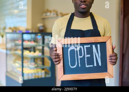 Gros plan sur un homme africain tenant un tableau noir avec un panneau ouvert entre ses mains, il ouvre son nouveau café Banque D'Images