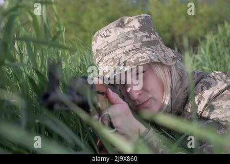 Soldat ukrainien féminin armé d'une carabine d'assaut posée dans l'herbe et visée Banque D'Images