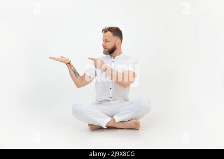 Beau homme sérieux avec tatouage s'asseoir sur le sol, blanc isolé fond. Gardez un espace vide à portée de main. Annoncer le produit Banque D'Images
