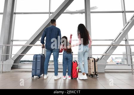 Famille avec fille regardant l'avion départ hors fenêtre à l'aéroport Banque D'Images