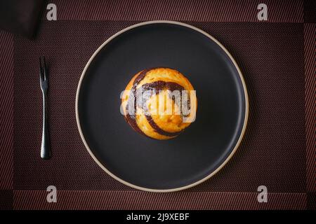 Muffin à la vanille au chocolat marbré sur papier brun isolé sur une fine assiette sur une table agréable, pâtisseries fines Banque D'Images