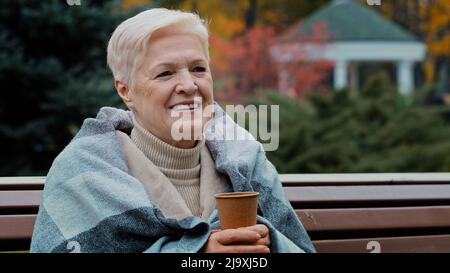 Bonne mature célibataire femme d'âge moyen couverte de chaud à boire du café chaud jetable tasse saine gai pensionné senior appréciant le repos Banque D'Images