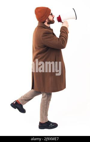 Prise de vue en studio verticale d'un homme barbu caucasien dans un manteau brun et un bonnet tenant le haut-parleur et annonçant les ventes à venir. Photo de haute qualité Banque D'Images