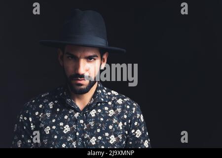 Homme barbu d'Amérique latine beau dans un chapeau noir regardant sévèrement dans l'espace de copie de caméra arrière-plan noir studio tourné moyen gros plan. Photo de haute qualité Banque D'Images