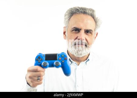Beau homme caucasien adulte avec des cheveux argentés et une barbe regardant l'appareil photo et tenant la manette de jeu bleue - isolé sur fond blanc. Photo de haute qualité Banque D'Images