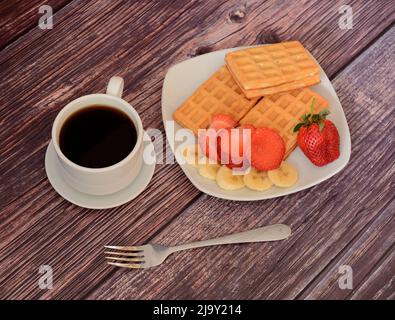 Des gaufres fraîches viennoises avec fraises et bananes sur un plateau, à côté d'une tasse de café noir sur une table en bois. Vue de dessus de la pose à plat. Banque D'Images