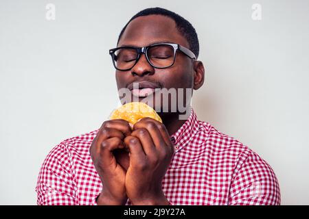 homme afro-américain appréciant le goût de hamburger.beau et jeune homme afro dans une chemise élégante et des verres tenant un hamburger sur un fond blanc Banque D'Images