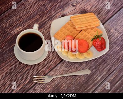 Des gaufres fraîches viennoises avec fraises et bananes sur un plateau, à côté d'une tasse de café noir sur une table en bois. Vue de dessus de la pose à plat. Banque D'Images