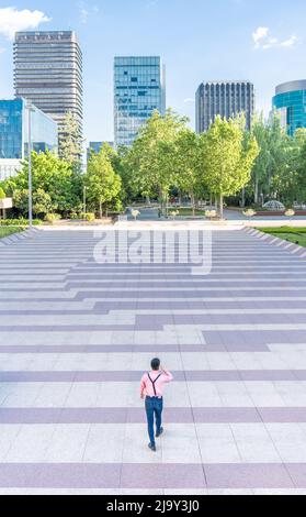 Homme marchant le long d'une place urbaine et des gratte-ciels en arrière-plan Banque D'Images