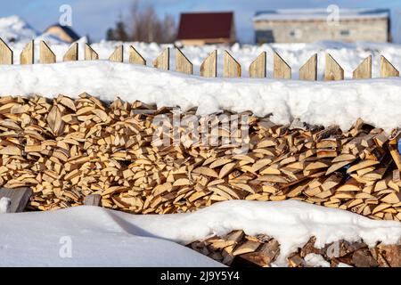 Bois de chauffage empilé dans une pile de bois le long d'une clôture en hiver sous la neige contre un ciel bleu. Préparation de bois de chauffage pour un bain et chauffage d'une maison Banque D'Images