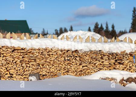 Bois de chauffage empilé dans une pile de bois le long d'une clôture en hiver sous la neige contre un ciel bleu. Préparation de bois de chauffage pour un bain et chauffage d'une maison Banque D'Images