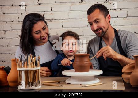 Jeune famille caucasienne heureuse avec son travail sur la boutique de potier. Belle mère avec papa et petit garçon faisant pot en céramique sur la classe d'art de poterie Banque D'Images