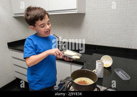 Enfant mettant un morceau de beurre dans la casserole avec du lait condensé et de la poudre de cacao. Banque D'Images