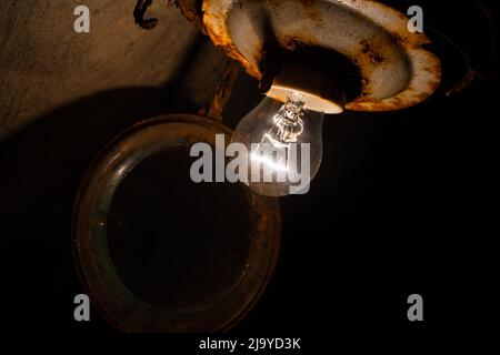 Une vieille ampoule à incandescence dans un ancien plafonnier rouillé dans un sous-sol sombre gros plan Banque D'Images