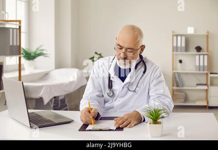 Ancien médecin de sexe masculin travaille sur ordinateur écrire sur la carte médicale Banque D'Images