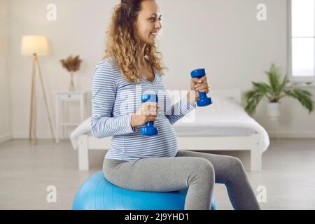 Belle et active jeune femme enceinte avec haltères et fitball faire de l'entraînement sportif à la maison Banque D'Images