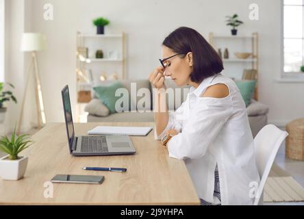 Femme fatiguée et fatiguée, assise au bureau avec ordinateur portable Banque D'Images