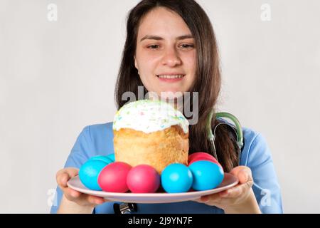 Le médecin tient un gâteau de Pâques et peint des oeufs et sourit sur un fond blanc. Banque D'Images