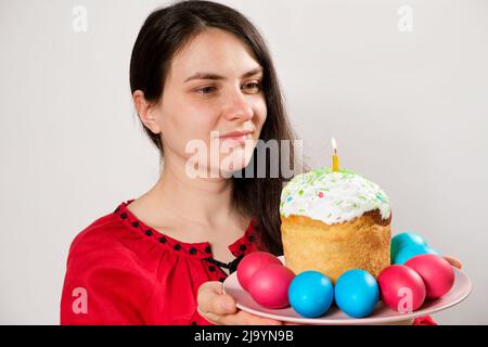 Une femme tient un gâteau de Pâques et des œufs peints sur un fond blanc, espace de copie pour le texte. Banque D'Images