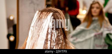 Belle jeune femme caucasienne avec de la feuille dans ses cheveux tout en teintant ses cheveux assis dans un salon de beauté Banque D'Images