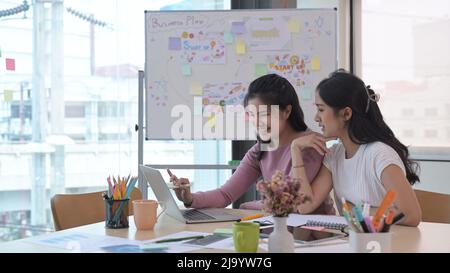 Photo de femmes entrepreneures heureuses utilisant un ordinateur portable tout en travaillant ensemble au bureau. Banque D'Images
