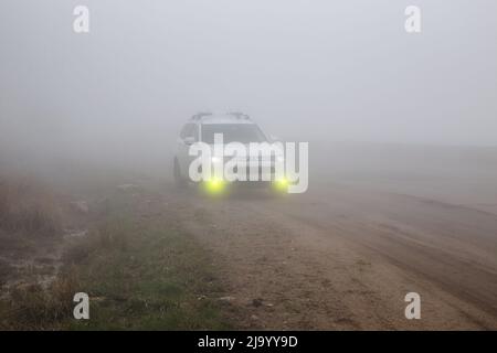 Col de GUM-Bashi, Nord Caucase, Russie - 07 mai 2022 : SUV multisegment Mitsubishi Outlander sur une route de montagne dans un brouillard épais avec des feux de brouillard Banque D'Images