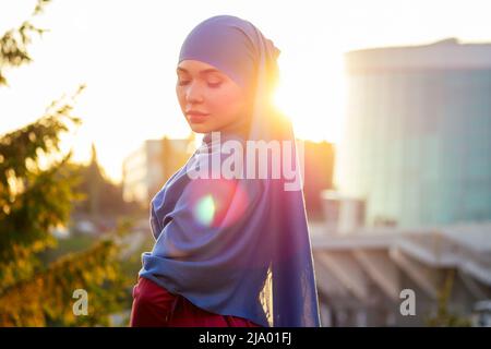 Portrait d'une belle femme musulmane aux yeux verts portant un foulard bleu visage fermé couvert d'aveil arrière-plan arbres forestiers dans le parc rayons du soleil Banque D'Images