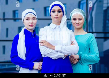 groupe de trois femmes d'affaires musulmanes femme caucasienne dans le hijab élégant et le turban travaillant sur les fenêtres de fond de bureau de rue d'un gratte-ciel Banque D'Images