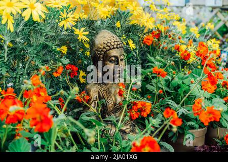 Statue décorative de Bouddha Gautama en bronze dans un jardin aux fleurs rouges et jaunes. Extérieur, concept de décor de jardin extérieur. Mise au point sélective Banque D'Images