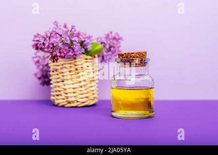 Huile cosmétique dans un pot et fleurs de lilas sur fond violet. Aromathérapie, concept de soins de la peau. Mise au point sélective. Banque D'Images