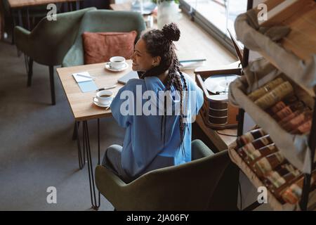 Vue de dessus sur jeune femme sportive gaie avec des tresses souriant tout en étant assis dans le café. Banque D'Images