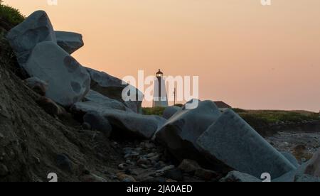Grands rochers sur la côte de Rhode Island avec le phare de point Junith et un ciel orange à l'aube en arrière-plan. Banque D'Images