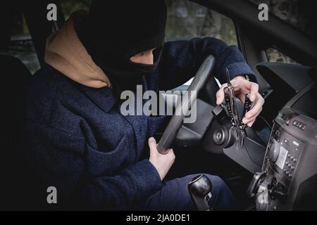 Un voleur de voiture dans un masque à l'exclusion de la reconnaissance, tente d'ouvrir la serrure d'allumage avec un outil. Crime, vol de voiture Banque D'Images