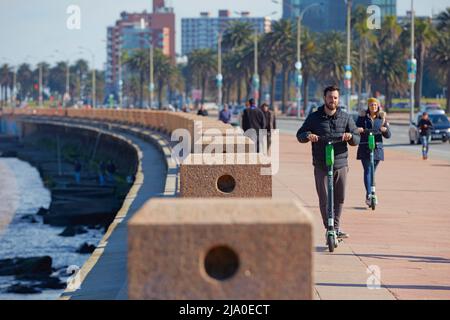 Deux jeunes sont en scooter électrique le long de la Rambla de Montevideo, en Uruguay. Banque D'Images