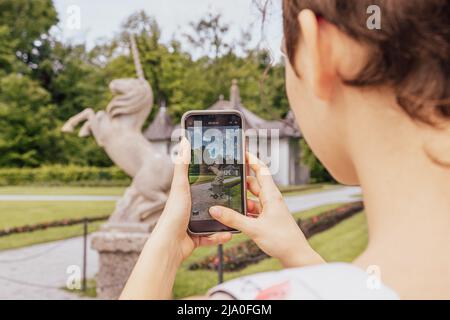 Une jeune fille méconnaissable à l'arrière prend des photos sur smartphone de monuments historiques, sculpture en pierre en forme de licorne, dans le parc Hellbrunn. Autriche, Banque D'Images