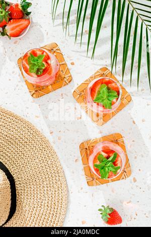 Eau d'été infusée à la menthe et aux fraises sur une table rose avec de longues ombres, vue du dessus Banque D'Images