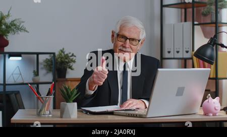 Un homme d'affaires senior lève le pouce, accepte, approuve, aime les bonnes nouvelles en utilisant un ordinateur portable au bureau à domicile Banque D'Images