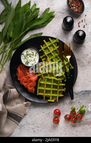 Gaufres belges vertes. Épinards ou ail sauvage ou gaufres au pesto avec saumon rouge et sauce à la crème sur fond de table en béton gris. Délicieux petit déjeuner, Banque D'Images