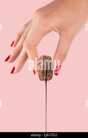 Macaron au chocolat sauce au chocolat tenue par une main manucure sur fond rose. Banque D'Images