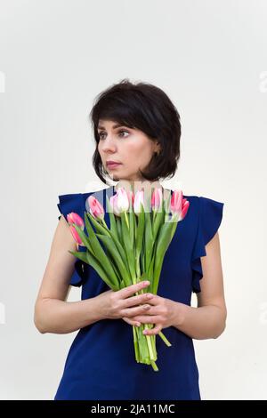 Portrait d'une femme adulte souriant brune de 40-45 ans avec bouquet de tulipes sur fond blanc. Banque D'Images