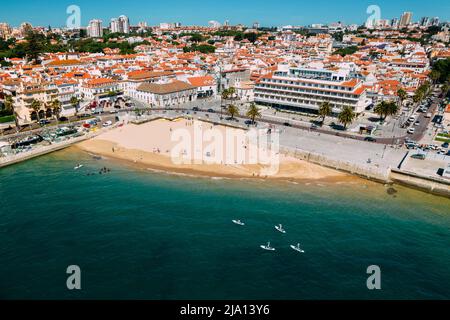 Vue aérienne du paysage urbain de Praia da Ribeira, Cascais, Portugal avec pagayeurs de stand-up au premier plan Banque D'Images