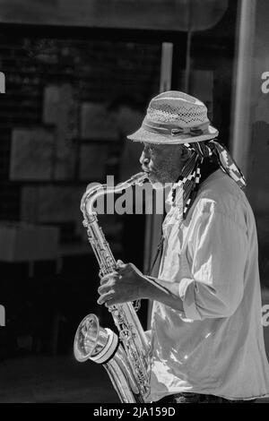 Portant une chemise décontractée et un chapeau de soleil, un homme joue le saxophone en plein air lors d'une journée ensoleillée à Leeds, West Yorkshire, Angleterre, Royaume-Uni. Banque D'Images