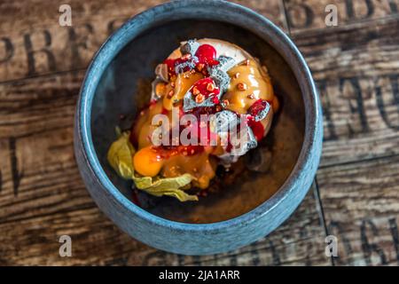 Un dessert composé de glace à la vanille, de morceaux de chocolat, de sauce au caramel et d'une sauce aux fruits rouges est servi au restaurant Pakkhús à Höfn, en Islande ; une physalis garnit l'assiette. Le restaurant est réputé pour ses spécialités à l'homard, capturés avec le bateau Sigurður Ólafsson. Banque D'Images