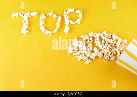 pop-corn dispersé sur un fond jaune avec inscription sur le dessus. Le concept des films à la maison et des films au cinéma. Pop-corn à base de grains de maïs Banque D'Images