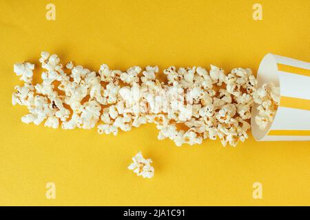 pop-corn diffusé à partir d'une tasse de papier à rayures sur fond jaune. le concept du home cinéma et des films au cinéma Banque D'Images