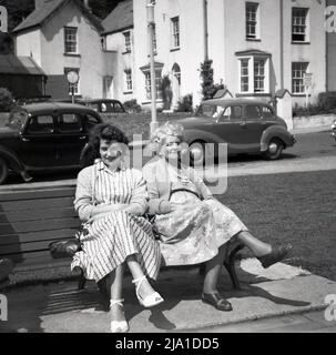 1950s, historique, une femme et sa mère portant les longues robes du jour, assis ensemble sur un banc, prenant l'air de la mer, Angleterre, Royaume-Uni. Voitures de l'époque garées sur le côté de la route. Banque D'Images