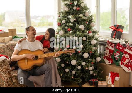 Le père et la petite fille s'amusent ensemble pendant les vacances de Noël. Papa joue de la guitare pour sa fille. Loisir d'un beau papa aimant avec lui Banque D'Images